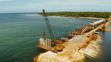 Kazık sürüş beton kazık yüklüyor. Ağır inşaat ekipmanları ve işçiler boğaz üzerinde bir köprü inşaatı. Siargao, Filipinler
