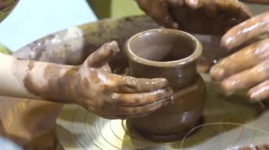 Bir çömlekçi, seramik tekerlekle çalışması için öğrencinin ellerine rehberlik ediyor. Çömlekçi çarklı çömlek atölyesi.