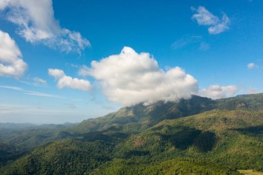 Mavi gökyüzüne karşı bulutlarla kaplı dağ zirveleri.