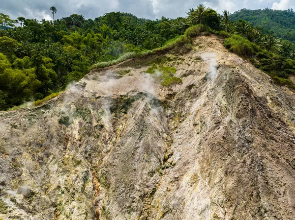 Aerial view of volcanic activity on a mountainside with smoke and escaping gases. Mag-Aso Volcanic Steam Spring. Negros, Philippines.