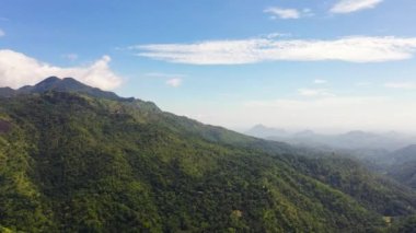 Aerial view of mountain slopes with green forest on the background of blue sky and clouds. Mountain landscape in Sri Lanka.