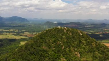 Tropikal bitki örtüsü olan bir vadinin arka planındaki dağın tepesindeki Budist manastırının insansız hava aracı. Sri Lanka.