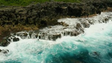 Adanın kıyı şeridi ve dalgalarla dalgalar kayalık bir sahile çarpıyor. Yavaş çekim, hava manzarası. Siargao, Filipinler. Yaz ve seyahat tatil konsepti