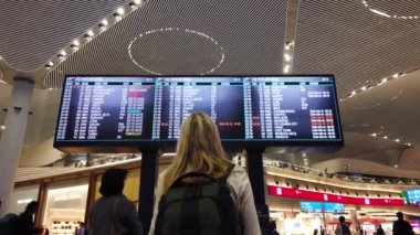 İstanbul Havaalanı - 27 Ekim 2019: Uluslararası havaalanında küçük sırt çantalı bir kadın uçuş bilgi panosuna bakıyor, uçuş bilgilerini kontrol ediyor.