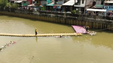 Kirli bir nehir, bir çöp kapanı ve nehri temizleyen işçiler. Jakarta, Endonezya.