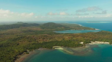 Deniz Burnu: Balabac adası kıyısı, orman ve palmiye ağaçları, turkuaz suyu olan mercan resifi, üst manzara. Yeşil ormanlarla kaplı tropikal adanın kıyı şeridi bulutlu mavi gökyüzüne karşı.