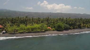 Siyah kumlu kıyı şeridi, palmiye ağaçları, otel, tropik tatil köylerindeki dağlar. Bali, Endonezya, seyahat konsepti. hava görüntüleri