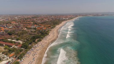 Dinlenen insanlar, oteller ve turistler, güneş şemsiyeleri, Bali, Kuta ile hava manzaralı kumsal. Su yüzeyindeki sörfçüler. Deniz manzarası, sahil, okyanus, gökyüzü deniz yolculuğu konsepti