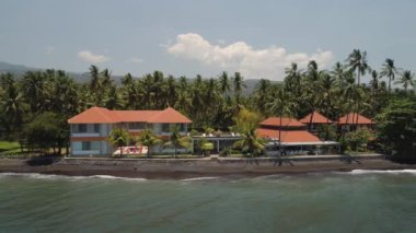 Havuzu, güneşli yatakları, deniz kenarında palmiye ağaçları olan lüks bir otel. Siyah kumlu sahil şeridi, palmiye ağaçları, otel, tropikal tatil köyü. Bali, Endonezya, seyahat konsepti. hava görüntüleri