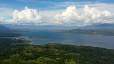 Yeşil tepeler ve yağmur ormanlarıyla kaplı dağların arasında mavi bir göl üzerindeki bulutlar. Hava manzaralı Pantabangan Gölü. Filipinler, Luzon.