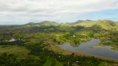 Dağların ve tepelerin arasındaki göl manzarası. Yağmur ormanları ve yeşil çimenler. Güneşli bir yaz gününde mavi gökyüzünün altında bulutlar. Bohol, Filipinler.