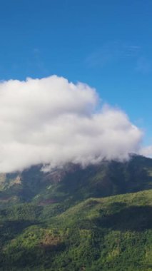 Aerial view of mountain peaks covered with clouds against the blue sky.