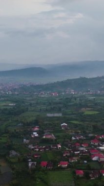 Gün batımında dağlık arazide çay tarlaları arasında şehrin havadan görünüşü. Kayu Aro, Sumatra, Endonezya.