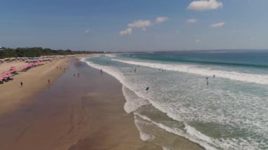 Dinlenen insanlar, oteller ve turistler, güneş şemsiyeleri, Bali, Kuta ile hava manzaralı kumsal. Su yüzeyindeki sörfçüler. Deniz manzarası, sahil, okyanus, gökyüzü deniz yolculuğu konsepti