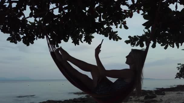 Жінка Лежить Гамаку Пляжі Приймає Селфі Під Час Заходу Сонця — стокове відео