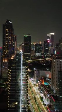 Jakarta şehrinin gökdelenli gece panoramasının insansız hava aracı. Dikey video.