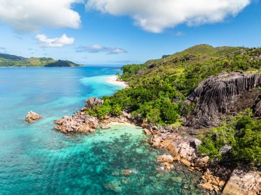 Tropik sahil manzarası, kayalık oluşumlar ve kıyı boyunca yemyeşil orman. Curieuse, Seyşeller.