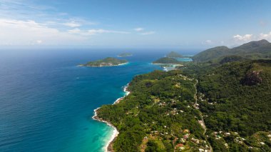 Kumlu plajları, turkuaz suları ve yoğun tropik yeşillikleri olan kıyı şeridi. Seyşeller, Mahe.