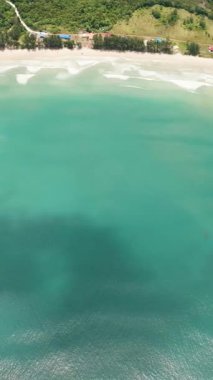 Temiz su ve deniz sörfü ile güzel kumlu sahil manzarası. Borneo, Malezya. Dikey video.