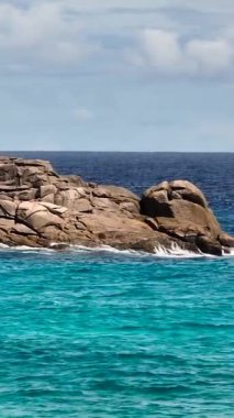 Kaya kıyısı, bulutlu bir gökyüzünün altında yemyeşil, canlı turkuaz dalgalarla çevrili. Seyşeller, Mahe.