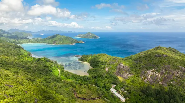Turkuaz koyları olan kıyı manzarası, yemyeşil tepeler ve bulutlu bir gökyüzünün altındaki uzak adalar. Seyşeller, Mahe.