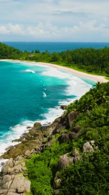 Berrak gök mavisi sular yemyeşil sularla çevrili beyaz kumlu bir kumsalla karşılaşır. Seyşeller, Mahe. Polis Körfezi.