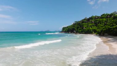 Plaj boyunca uzanan beyaz kumlar berrak, sakin sular ve yemyeşil sularla buluşur. Seyşeller, Mahe. Anse Louis Sahili.