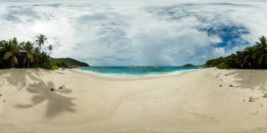 Palmiye ağaçları, turkuaz dalgalar ve parçalı bulutlu bir gökyüzünün altındaki kayalık adalarla kaplı güzel kumlu bir sahil. Anse Petit Boileau, Seyşeller. 360VR.