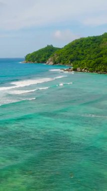 Turkuaz okyanus dalgaları kayalık sahil şeridi boyunca uzanan tropikal bir ormanın yemyeşil sularıyla karşılaşıyor. Seyşeller, Mahe.