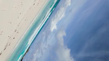 Turkuaz dalgalar, parlak bir gökyüzünün altında beyaz kumlu kıyıya çarpıyor. Uzakta kayalık oluşumlar var. Seyşeller, La Digue. Anse Komandoları.