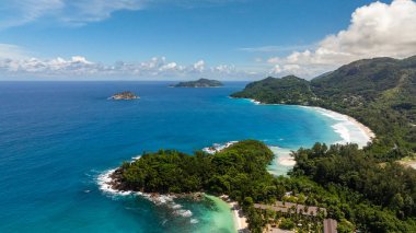 Berrak bir gökyüzünün altında canlı turkuaz sularla çevrili yemyeşil yemyeşil bir ada. Seyşeller, Mahe.