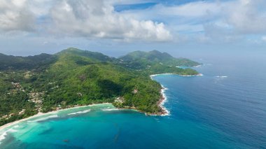 Turkuaz sular, yeşil tepeleri çevreleyerek okyanusa doğru uzanır ve küçük dalgalar kıyıya vurur. Seyşeller, Mahe.