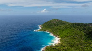 Kıyı şeridi tepelerle kaplı ve turkuaz sulara bakan yoğun bitki örtüsüyle kaplı. Seyşeller, Mahe.