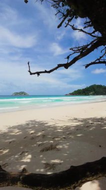 Açık turkuaz okyanus, küçük uzak bir ada ve kumlu bir sahilden görünen mavi gökyüzü. Büyük Anse. Seyşeller, Mahe.