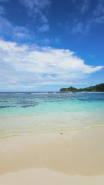 Temiz turkuaz su, bulutlu bir gökyüzünün altında, arka planda yemyeşil yemyeşil ile beyaz kumlu plajla buluşur. Seyşeller, Mahe.