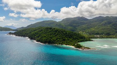 Bereketli yeşil kıyı tepeleri, beyaz kumlu ve kayalık oluşumları olan turkuaz sularla karşılaşıyor. Seyşeller, Mahe.