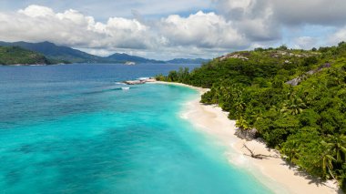 A white sandy beach with clear turquoise water, bordered by dense green vegetation. Therese. Seychelles, Mahe. clipart