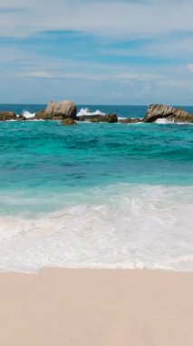 Canlı turkuaz dalgalar ufukta kayalık çıkıntılarla yavaşça kıyıya çarpıyor. Seyşeller, Mahe. Anse Boileau.