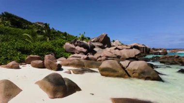 Bereketli tropik yeşillik ve turkuaz sularla çevrili beyaz kumlu bir sahilden granit kayalar yükseliyor. Anse Cocos. Seyşeller, La Digue.