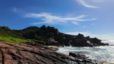 Kıyı şeridi boyunca yeşil yapraklı granit kayalar ve kıyıya vuran dalgalar. Seyşeller, La Digue.