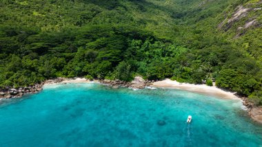 Berrak turkuaz suyu olan bir plajın yanındaki sık tropikal ormanda yuva yapmış granit kayalar. Anse Major. Seyşeller, Mahe.