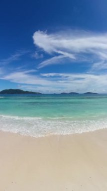 Yumuşak beyaz kum kristal berraklığında turkuaz okyanusla buluşuyor. Dalgalı mavi gökyüzünün altında, dağınık bulutlarla. Seyşeller, La Digue.