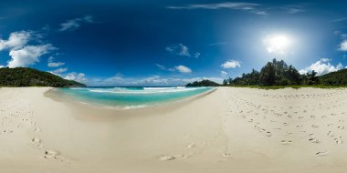 Canlı bir gökyüzünün altında yemyeşil tepeler ve yeşilliklerle çevrili turkuaz okyanusun yumuşak dalgalarına doğru giden huzurlu kumlu bir sahil. Polis Körfezi. Mahe, Seyşeller. VR 360.
