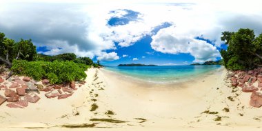 Parlak bir gökyüzü altında pürüzsüz kayalar, kristal sular ve canlı yeşilliklerle el değmemiş bir sahil sahnesi. Praslin, Seyşeller. Anse Takamaka. 360 görünüm.