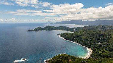 Bereketli bir sahil şeridinin panoramik manzarası. Mavi gökyüzünün altında tepeler ve turkuaz sular. Seyşeller, Mahe.