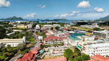 Binalar, liman, rüzgar türbinleri ve açık bir gökyüzünün altındaki uzak dağlarla dolu bir şehir manzarası. Seyşeller, Mahe. Victoria..