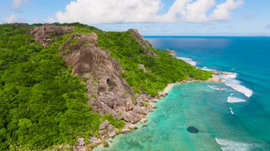 Uçurum kenarındaki granit oluşumlar, turkuaz okyanus sularıyla tropik bir manzarada buluşur. La Digue, Seyşeller.