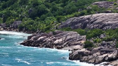 Sahildeki dalgaların üzerinde yemyeşil tepeler yükseliyor. Seyşeller, Felicite.