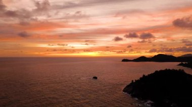 Parlayan bulutlarla gün batımı sahnesi, sakin bir okyanus, ve ada siluetleriyle uzak bir ufuk. Seyşeller, Mahe.