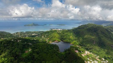 Okyanusa bakan yemyeşil tepeler, uzaktaki küçük bir adanın manzarası. Seyşeller, Mahe.